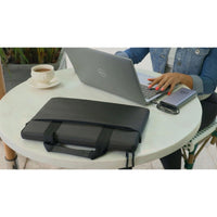 A user at a cafe with the Dell EcoLoop Black Sleeve Case for 11-14 Inch Notebooks resting on the table, emphasizing its sleek design and functionality in a casual environment.