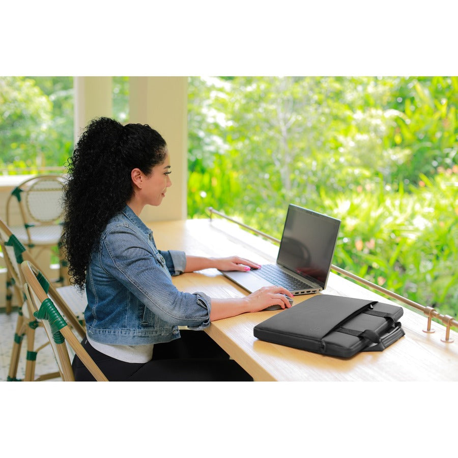 A woman using a laptop at a workspace with the Dell EcoLoop Black Sleeve Case for 11-14 Inch Notebooks beside her, highlighting the blend of style and practicality.