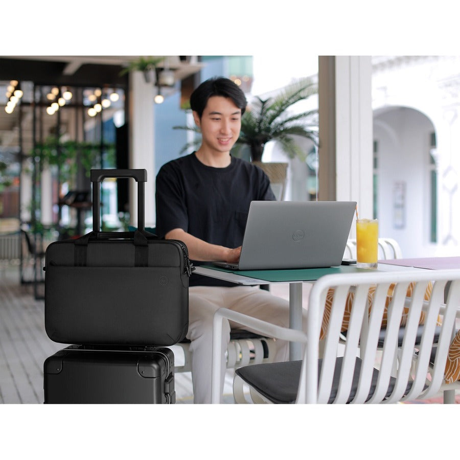 A young professional working on a laptop with the Dell EcoLoop Pro 16" Notebook Carrying Case beside them, illustrating its compatibility and convenience in a café setting.