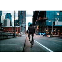 A cyclist commuting through a cityscape at dusk, showcasing the Dell EcoLoop 14-16In Backpack, designed for sustainability and durability.