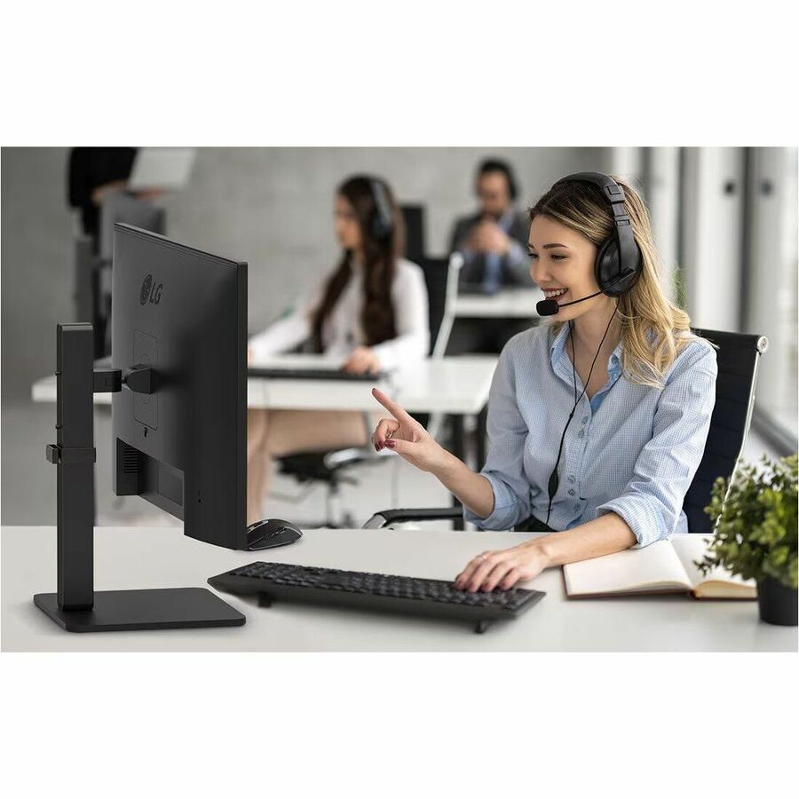 A professional setting with a woman engaging with her LG 27BA550B 27 FHD IPS Monitor featuring a 100Hz refresh rate, ergonomic design, and built-in speakers.