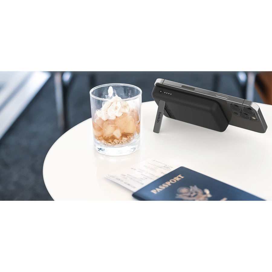Belkin MagSafe Power Bank 5K placed on a table with a cocktail, emphasizing its stylish look and functionality.