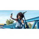 A woman with curly hair enjoying a selfie while charging her phone with the Belkin MagSafe Power Bank 5K. The power bank ensures seamless wireless charging, showcasing its stylish compact design.