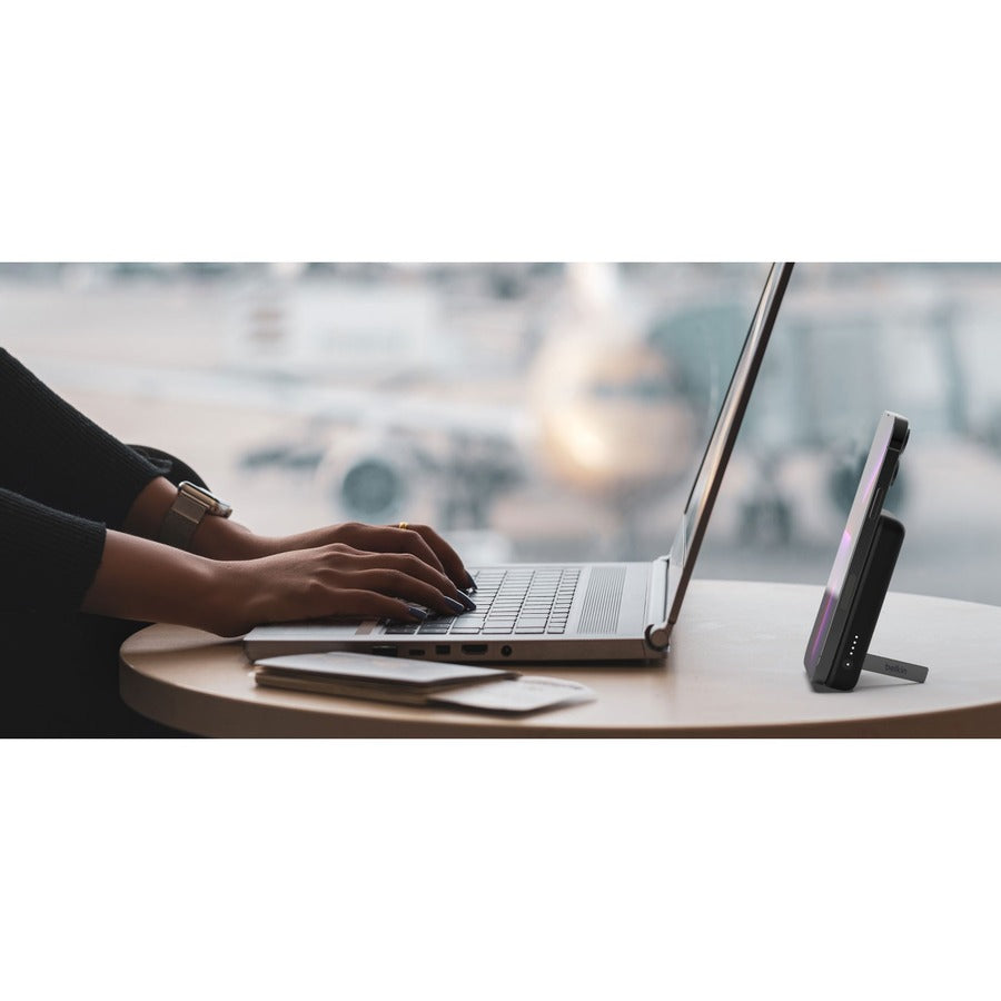 A close-up of a laptop and the Belkin MagSafe Power Bank 5K with a pop-up kickstand, optimized for hands-free usability. The elegant setup highlights the power bank's efficiency and convenience in a professional setting.